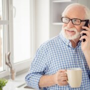 Close up portrait grey haired he his him grandpa hot beverage hand arm tell children health condition telephone smart phone user wear specs casual checkered plaid shirt jeans denim outfit room kitchen